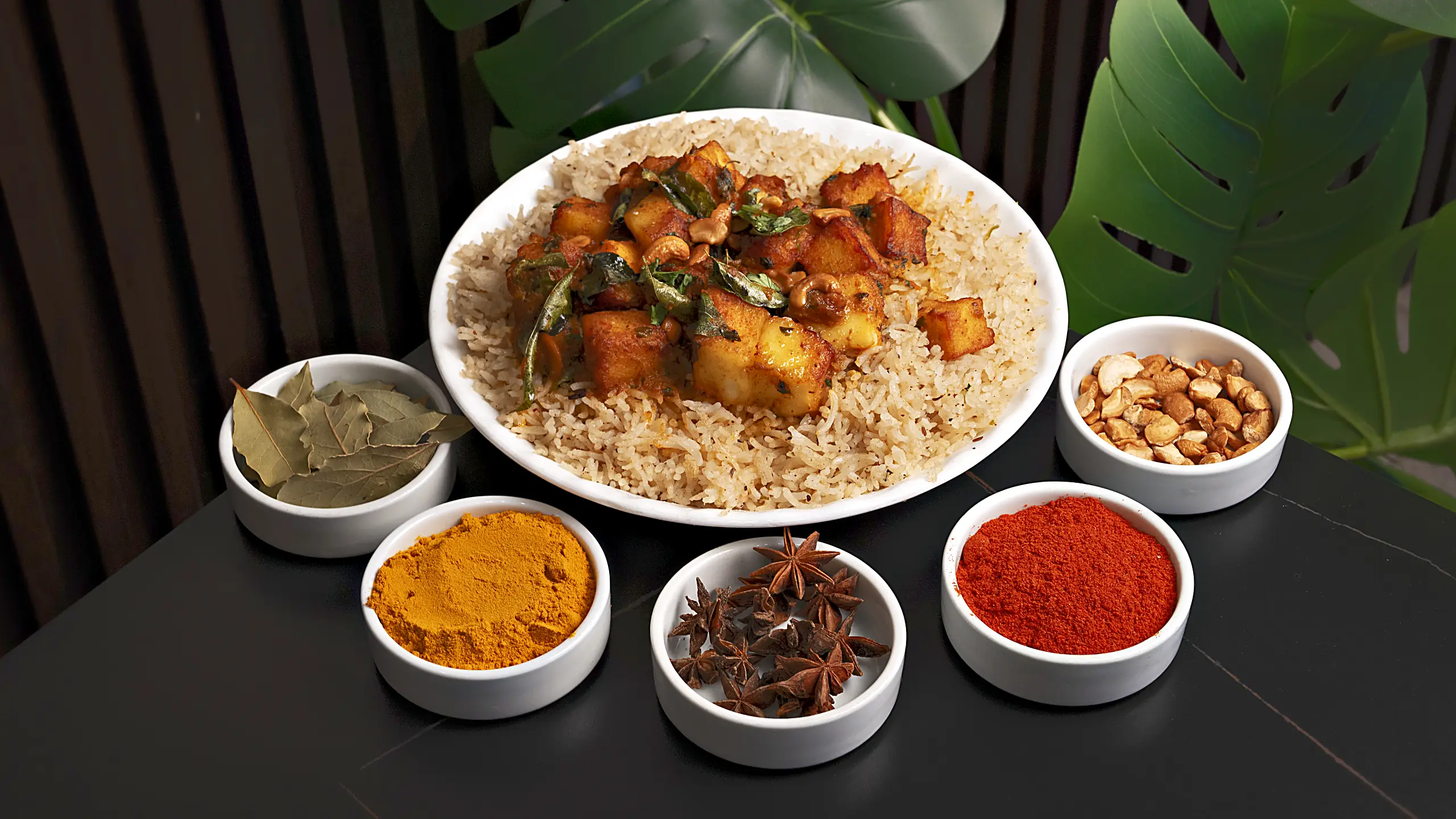 Plate of mandi rice topped with spiced paneer and curry leaves, with small bowls of bay leaves, turmeric, star anise, chilli powder and cashews