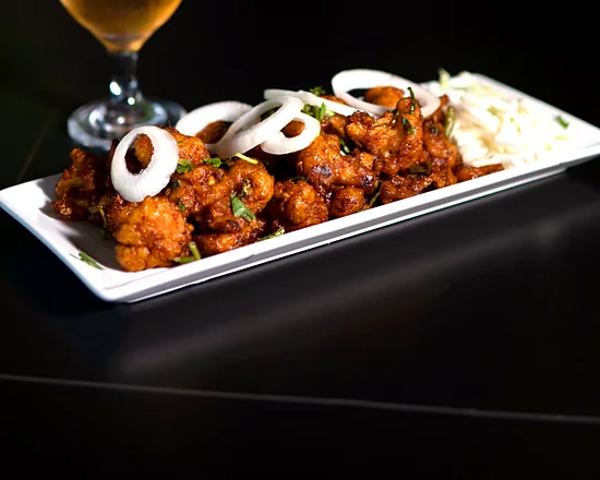 Chicken 65 on a white platter with onion rings and shredded cabbage