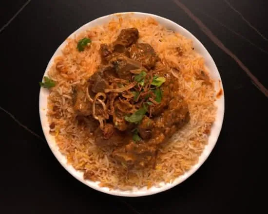 Plate of mutton biryani topped with mutton masala, fried onions and coriander